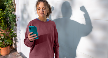 young female adult looking at her mobile device with her shadow behind her flexing her arm muscles