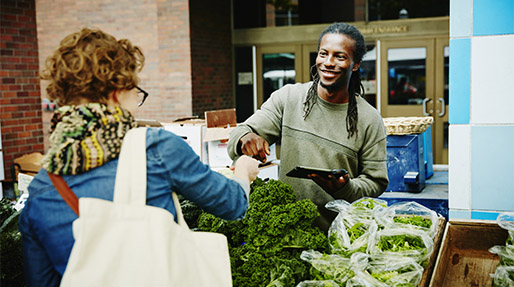 Black man taking payment after selling vegetables to a woman at a farmers market
