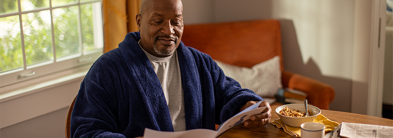 older black man eating breakfast while reading his health insurance benefits handbook