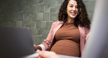pregnant women sitting by her laptop computer smiling