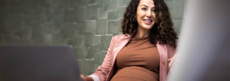 pregnant women sitting by her laptop computer smiling