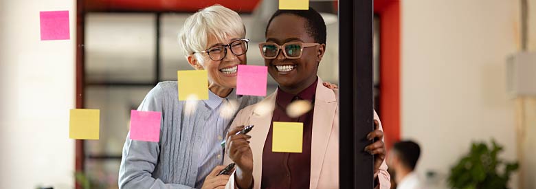 two women adding post it stickies to a glass wall