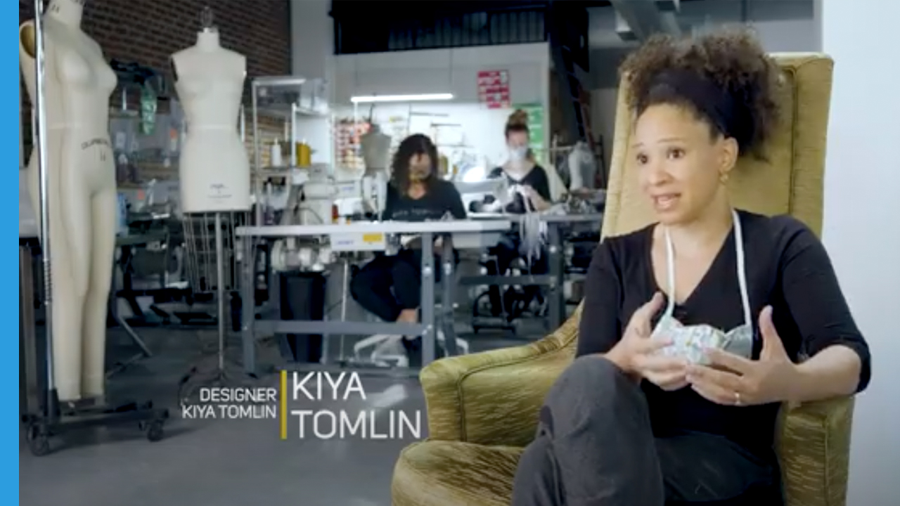 Deisgner Kira Tomlin sitting in a chair talking with sewing machines behind her
