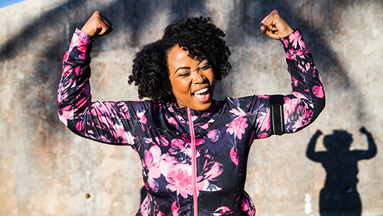 woman in workout gear smiling with arms raised in victory