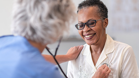 woman in glasses being checked with a stethoscope by female doctor