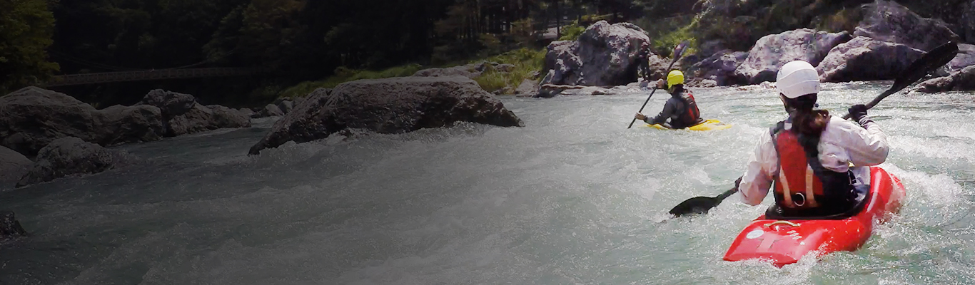 two people in life jackets, helmets, gloves, paddling down raging river rapids in kayaks.