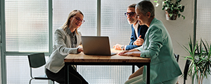 a medicare specialist sitting with two people explaining medicare to them while also looking at a laptop computer