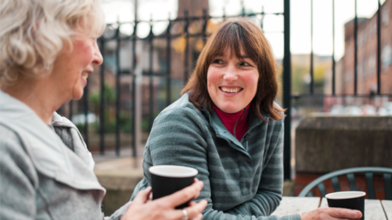 two woman sitting outside talking and drinking coffee