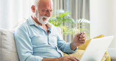 older man sitting on a couch smiling and navigating on his laptop computer