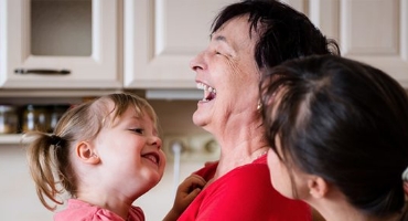 Grandmother and toddler laughing together in the kitchen as mother looks on, all might benefit from Highmark Medicare Plans