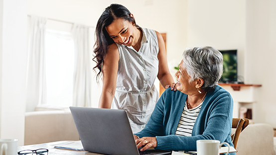 two women, one sitting at a desk with a laptop computer and the other standing next to her