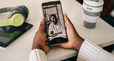 A person holding a mobile device having a virtual appointment with a mental health provider.