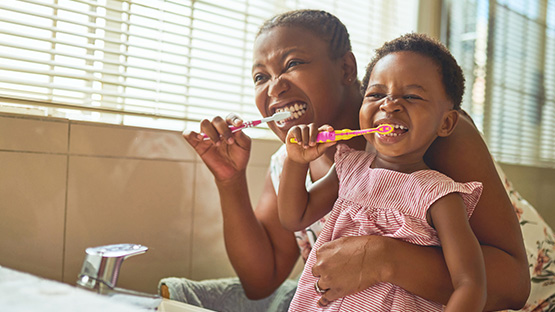 mother holding toddler daughter while both brushing their teeth