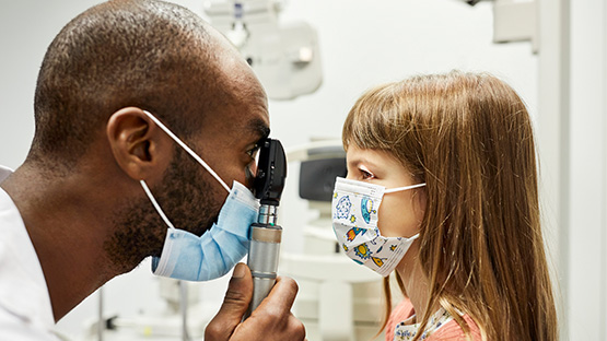 Male doctor looking into a female child's eye with a hand held Ophthalmoscope