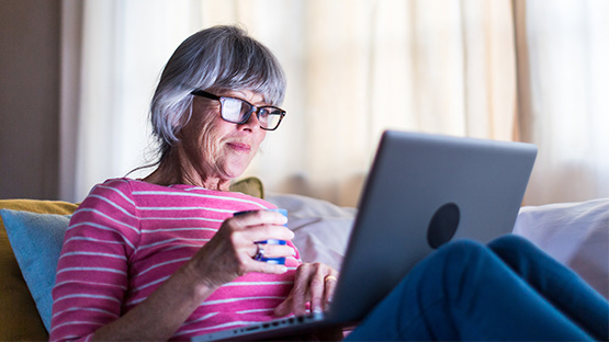 Senior woman sitting on couch with laptop  on lap reading it