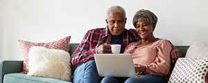 Senior couple sitting on couch reading a laptop on their lap